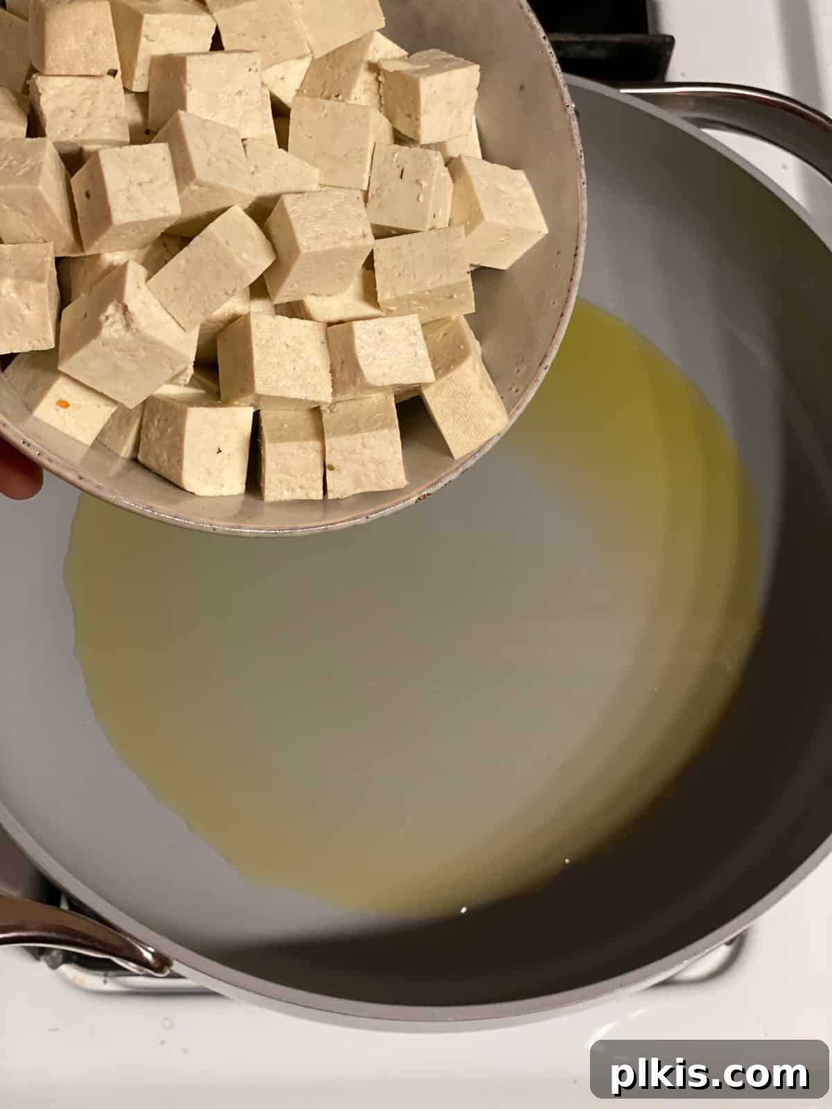 Creamy Red Curry Tofu: Slow Cooker or Stove Top 4 Tofu cubes being carefully added to a hot skillet with oil, showing the initial stage of pan-frying for Slow Cooker Red Thai Curry.
