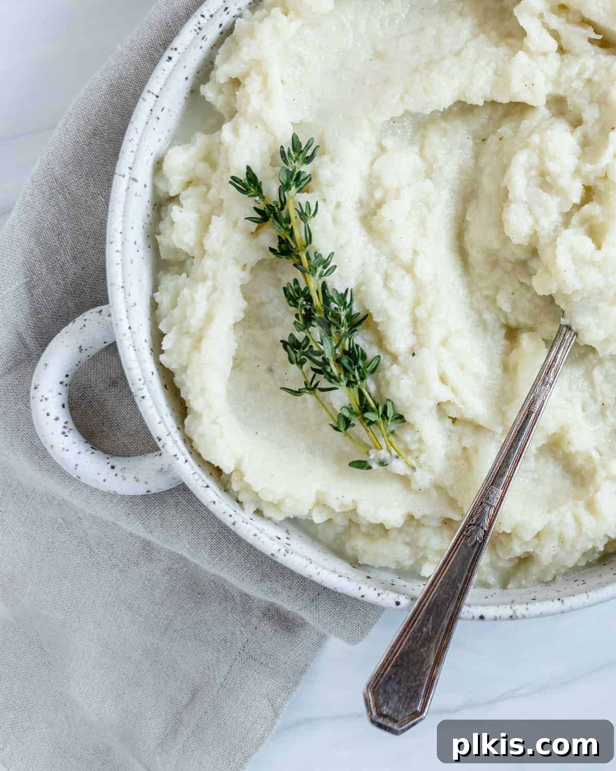 Creamy Vegan Mashed Cauliflower Keto Low Carb 7 completed mashed cauliflower in a white dish with a spoon in the mashed cauliflower against white background