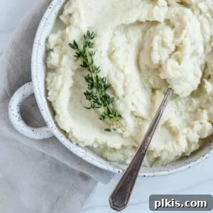 Creamy Vegan Mashed Cauliflower Keto Low Carb 8 completed mashed cauliflower in a white dish with a spoon in the mashed cauliflower against white background