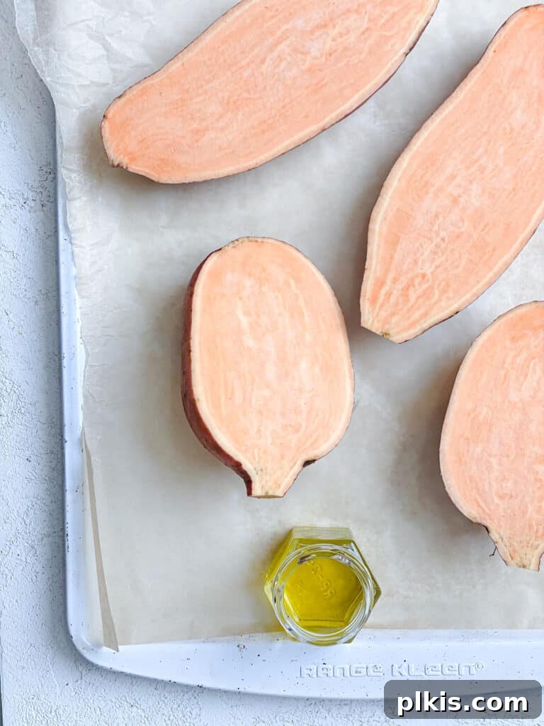 Sliced sweet potatoes, brushed with oil, arranged cut-side up on a baking tray, ready for roasting.