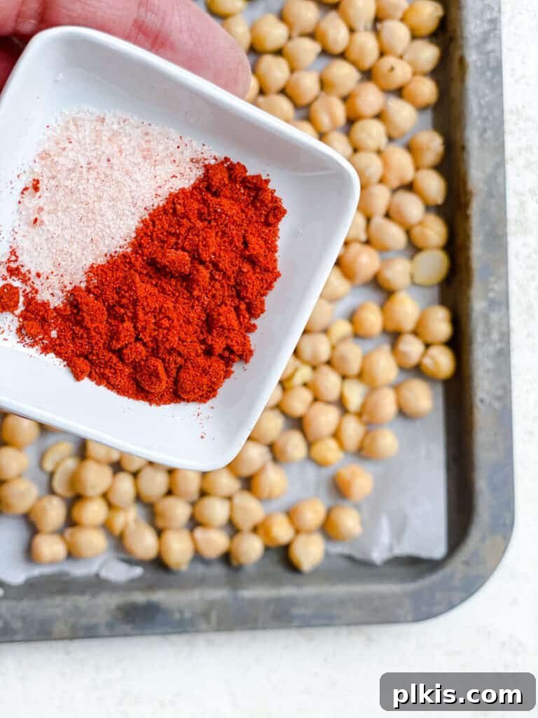 Process shot of adding salt and paprika spices to drained chickpeas spread on a baking tray.
