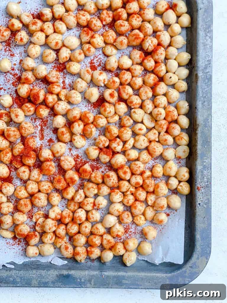 Process shot of mixing chickpeas and spices thoroughly on a baking tray to ensure even coating before roasting.