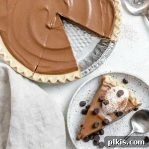 completed Chocolate Pumpkin Pie against a white surface with a slice missing and plated in the background
