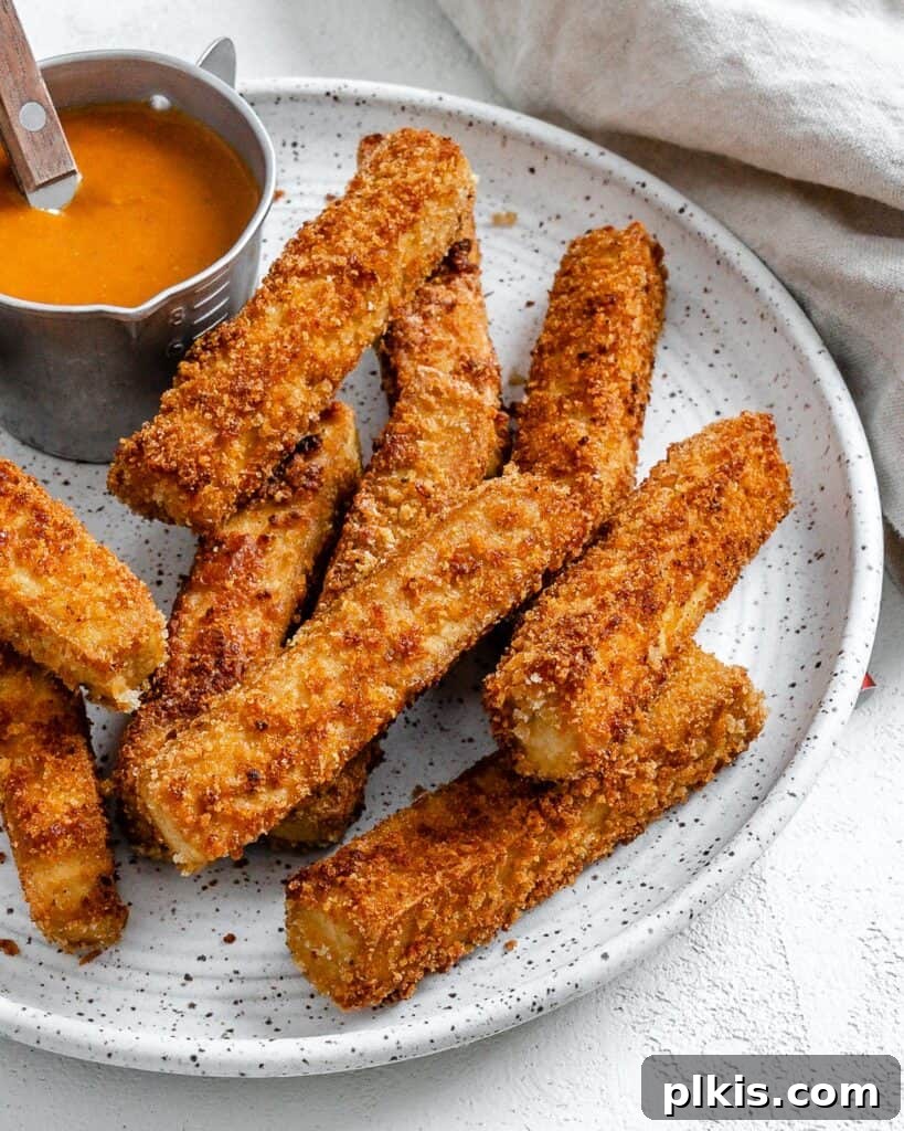 Crispy vegan breaded tofu strips served on a white plate with a side of savory dipping sauce, ready to be enjoyed.