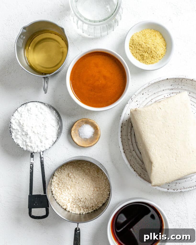 Individual ingredients for vegan breaded tofu strips, including a block of tofu, cornstarch, soy sauce, nutritional yeast, and breadcrumbs, neatly arranged against a white background.