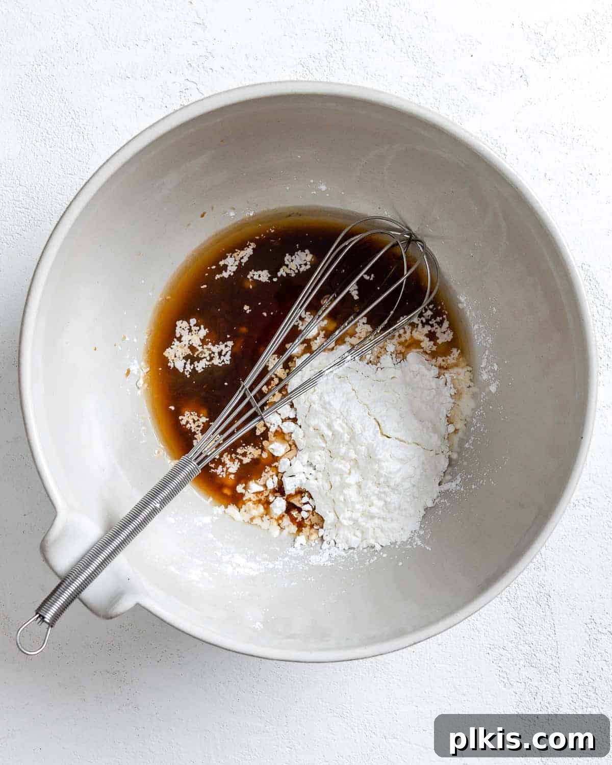 The process of combining cornstarch, water, and soy sauce in a white bowl to create the slurry for breaded tofu.