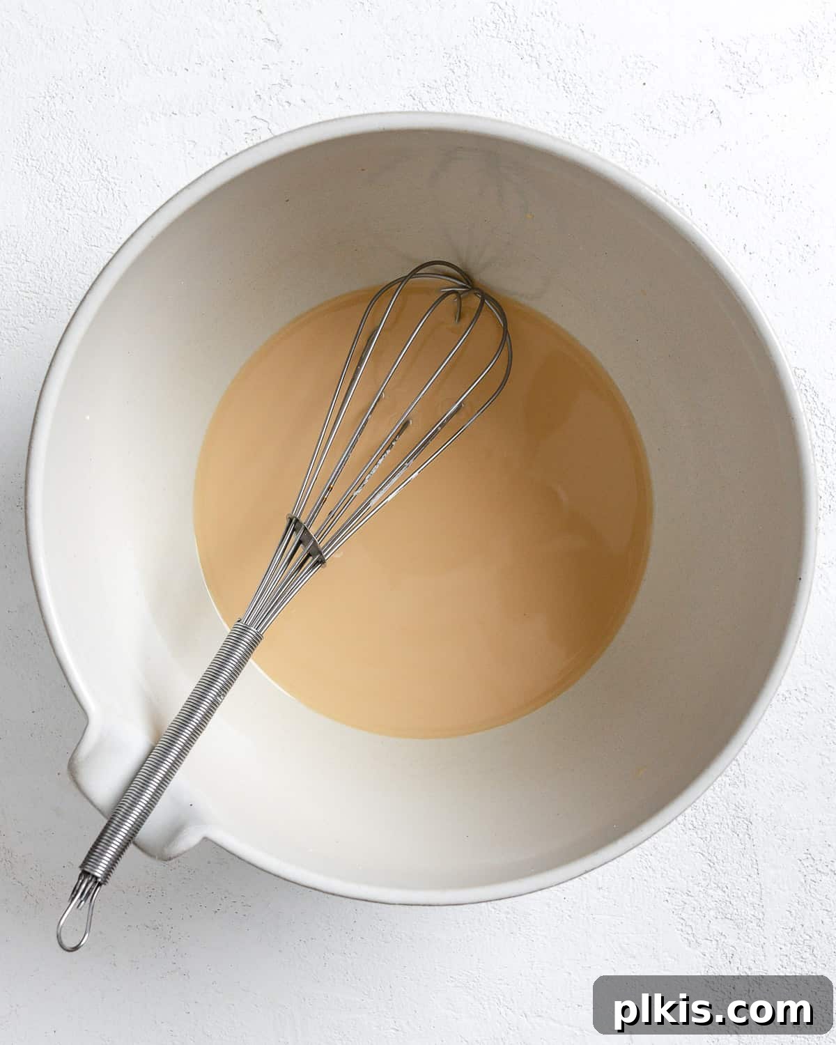 A smooth, whisked cornstarch slurry ready for coating tofu, in a white bowl against a white background.