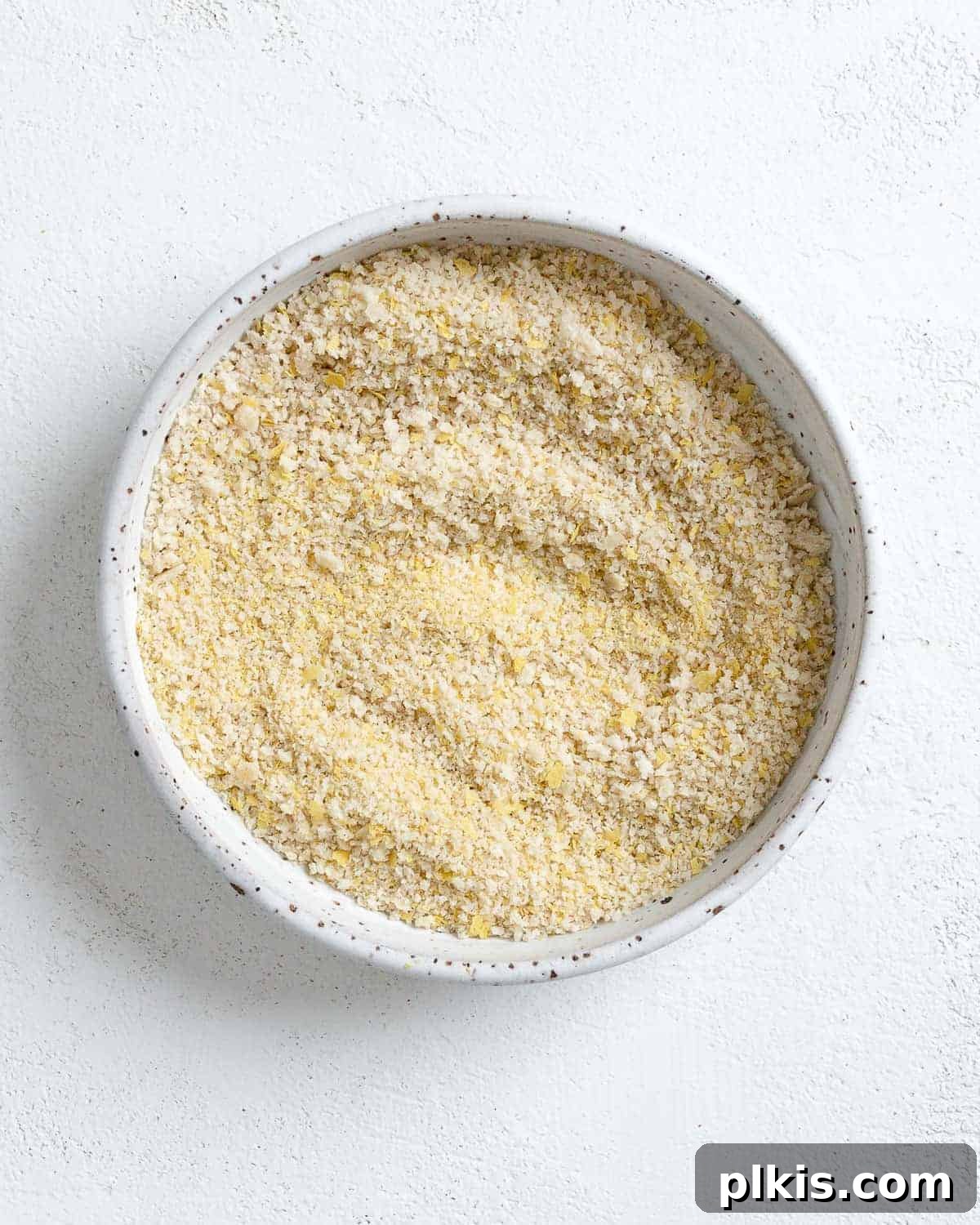 The fully mixed breading combination of breadcrumbs, nutritional yeast, and salt on a white plate, ready for tofu coating.