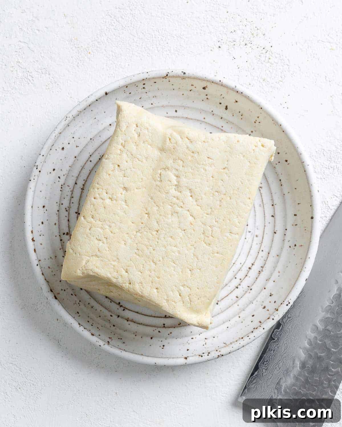 Zesty Tofu Tacos 4 A block of firm tofu ready for preparation on a small white plate, highlighting the main ingredient for the tacos.