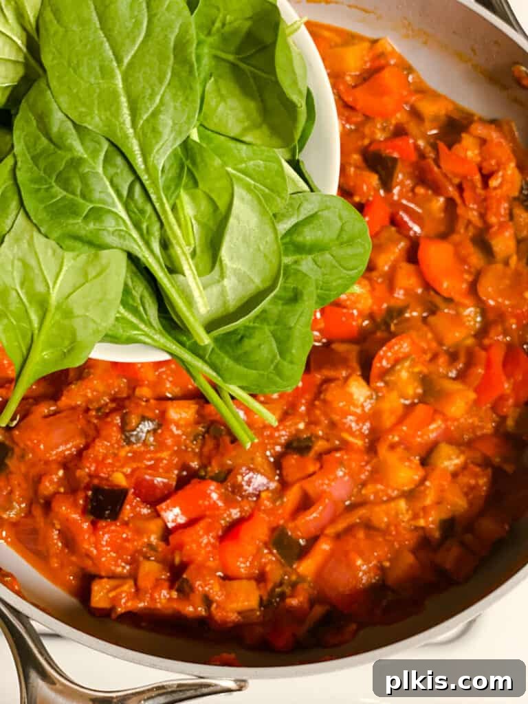 Effortless Eggplant Penne Alla Norma 11 Process shot of adding fresh spinach to the simmering tomato and vegetable sauce.