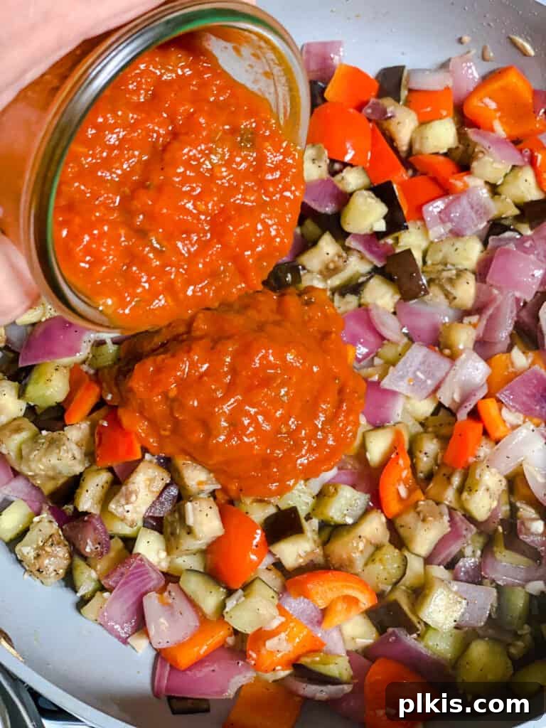 Effortless Eggplant Penne Alla Norma 10 Process shot of adding tomato sauce to the cooked vegetables in the pan.