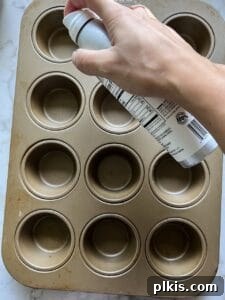 Effortless Vegan Blueberry Banana Delights 4 A hand spraying oil into a muffin tin tray, preparing it for baking.