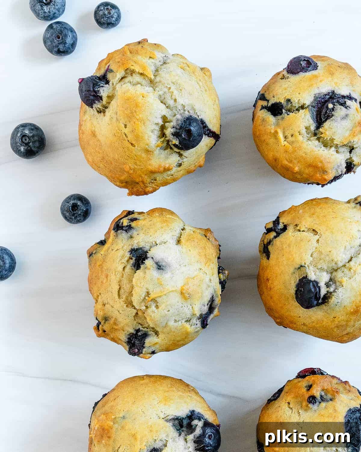 Effortless Vegan Blueberry Banana Delights 7 Close-up of baked vegan blueberry banana muffins on a white surface with scattered fresh blueberries in the background.