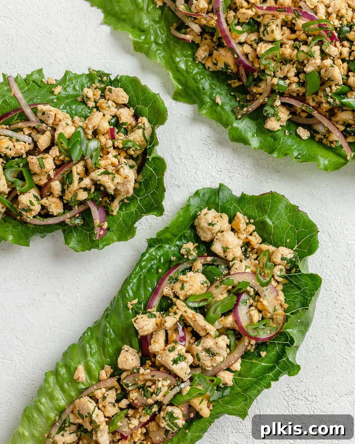 Vibrant Vegan Tofu Larb 2 Three completed larb salad servings against a white surface, garnished with fresh herbs and lime.