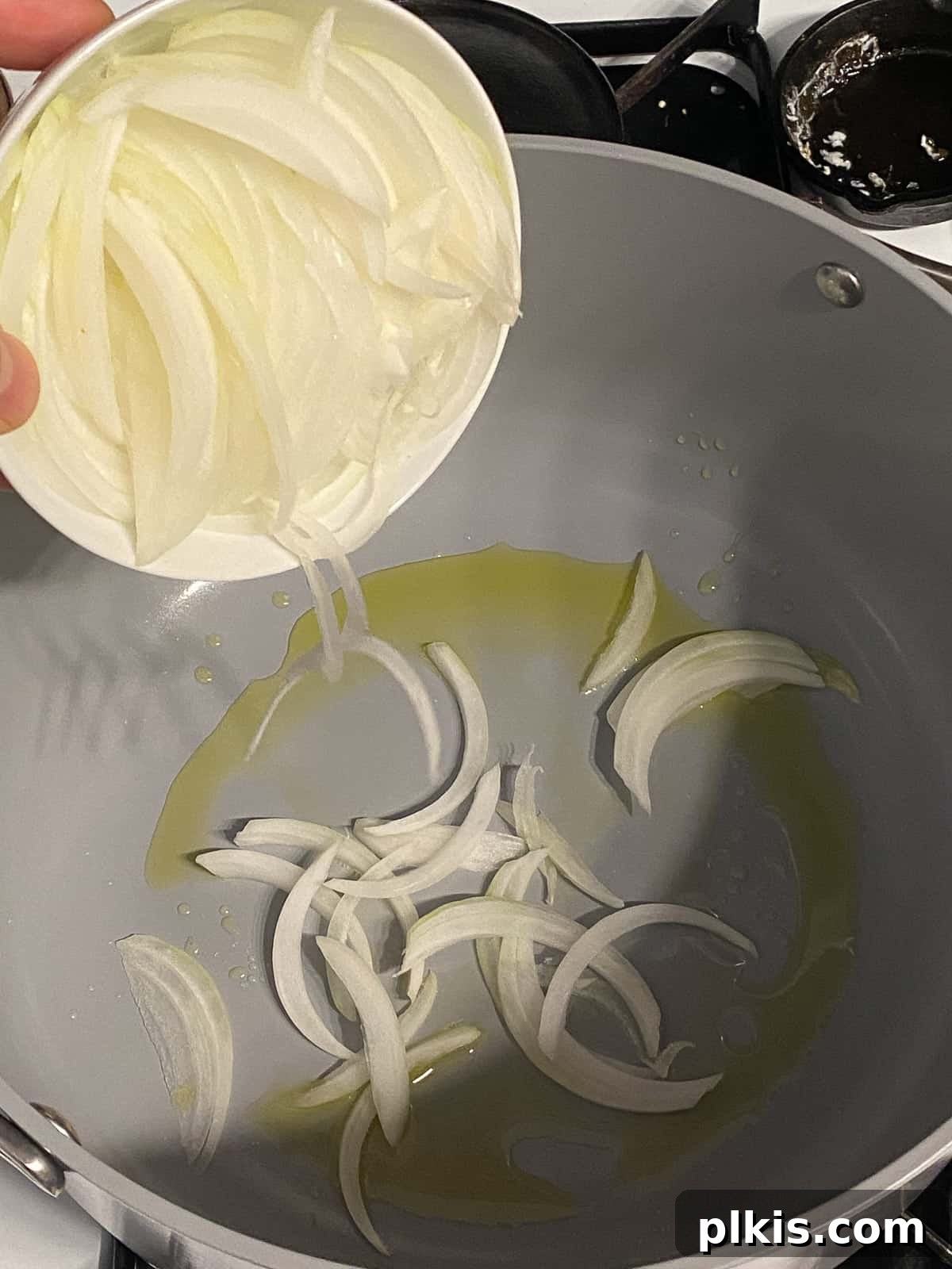 Wholesome Vegan Tofu Broth 4 Process shot of thinly sliced yellow onions being poured into a large pot with heated oil, ready for sautéing to form the flavor base of the Caldo de Tofu.