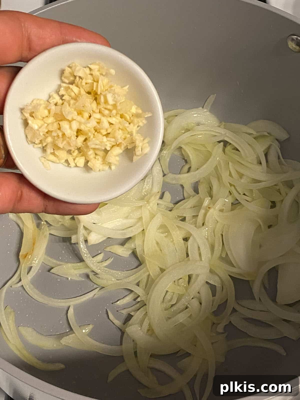 Wholesome Vegan Tofu Broth 5 Close-up process shot showing minced garlic being added to the sautéing onions and other vegetables in a large pot, enhancing the aromatic foundation of the Caldo de Tofu.
