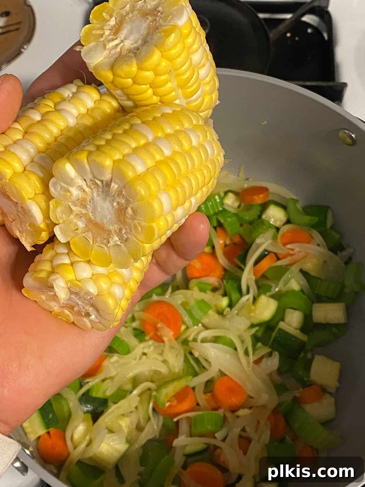 Wholesome Vegan Tofu Broth 7 Process shot of adding fresh corn on the cob, cut into thirds, into the pot with sautéed vegetables, preparing for the next stage of Caldo de Tofu.