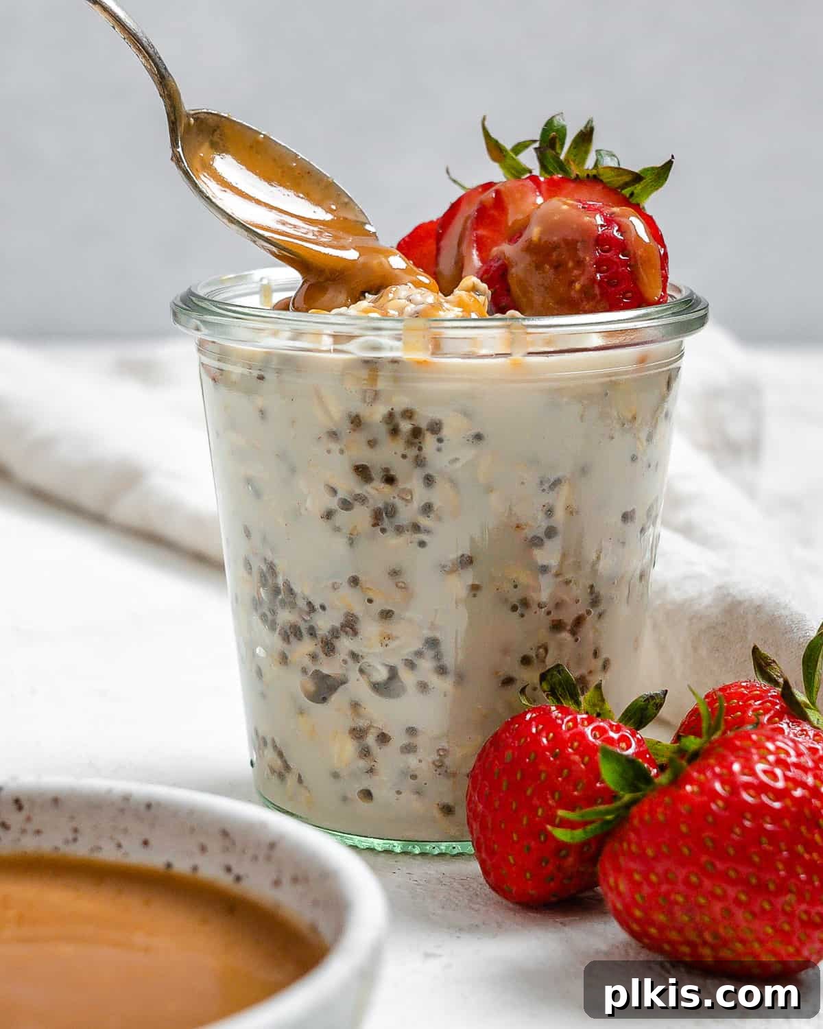 Decadent Salted Caramel Overnight Oats 12 completed Salted Caramel Overnight Oats in a clear cup with ingredients against a white background