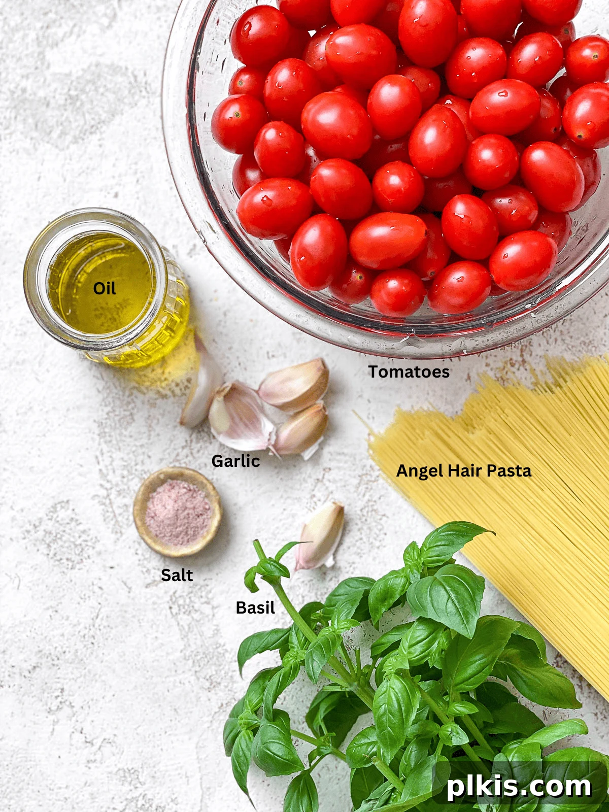 Cherry Tomato Basil Pasta in 15 Minutes 3 A selection of fresh ingredients laid out on a white surface, including cherry tomatoes, garlic, basil, pasta, and olive oil.