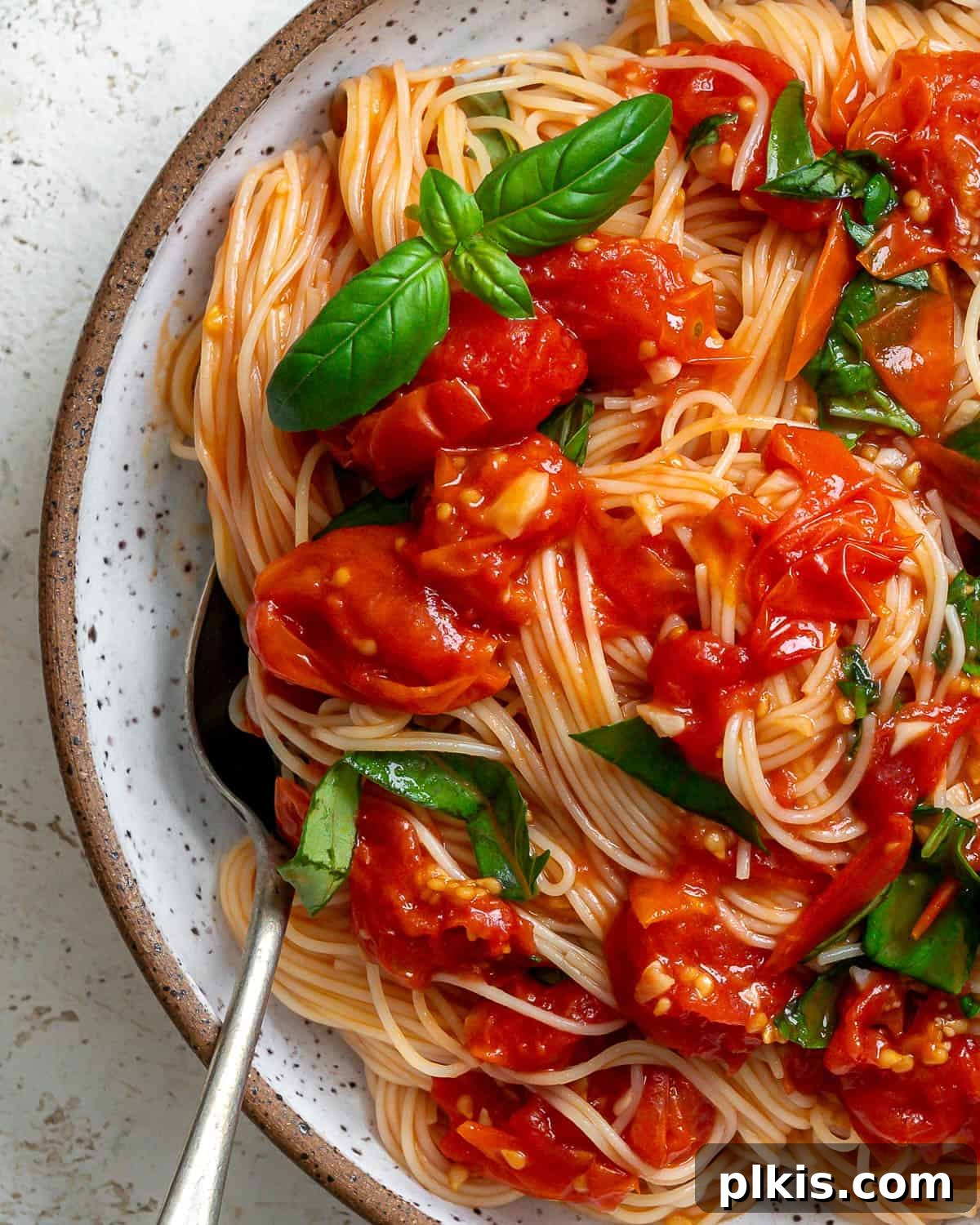 Cherry Tomato Basil Pasta in 15 Minutes 7 A close-up shot of a serving of Cherry Tomato Basil Pasta in a white bowl, garnished with fresh basil leaves.