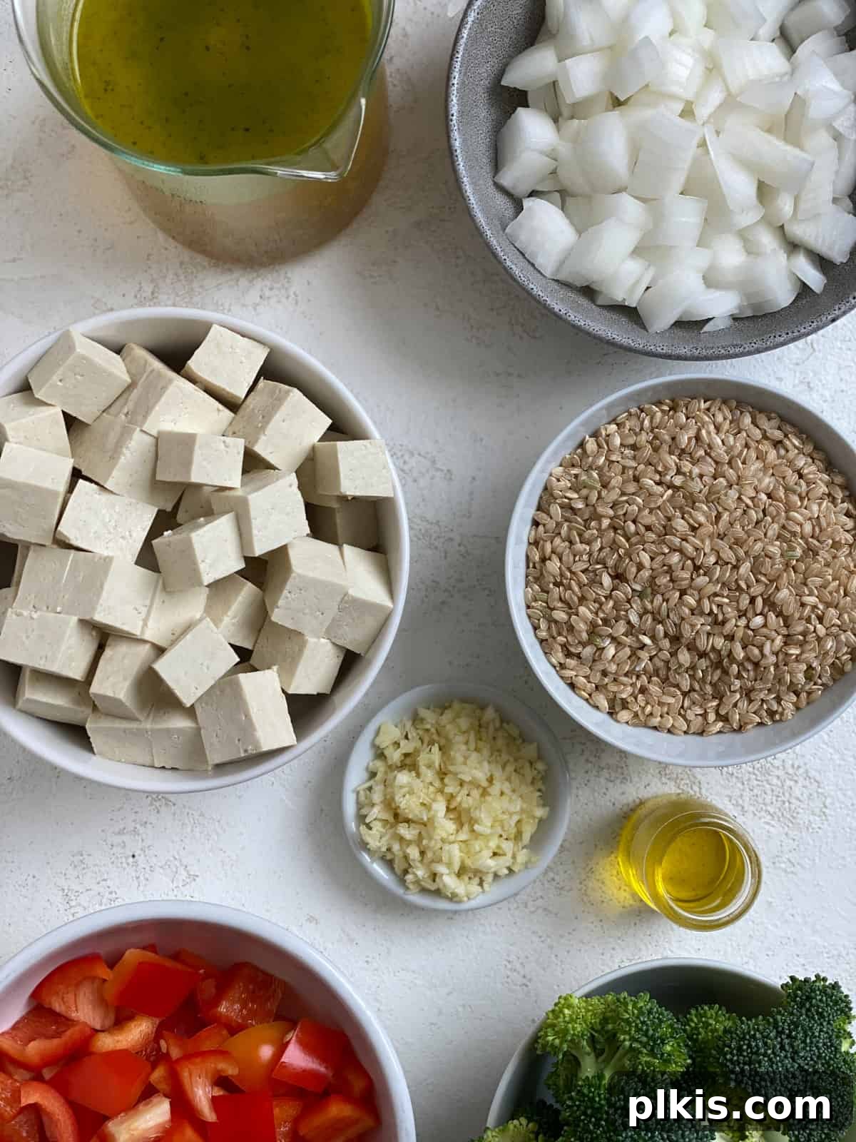 Vibrant Veggie Brown Rice Stir Fry 3 Fresh ingredients laid out for Veggie Brown Rice Stir Fry, including uncooked brown rice, crisp vegetables, and firm tofu cubes, ready for preparation against a white background.