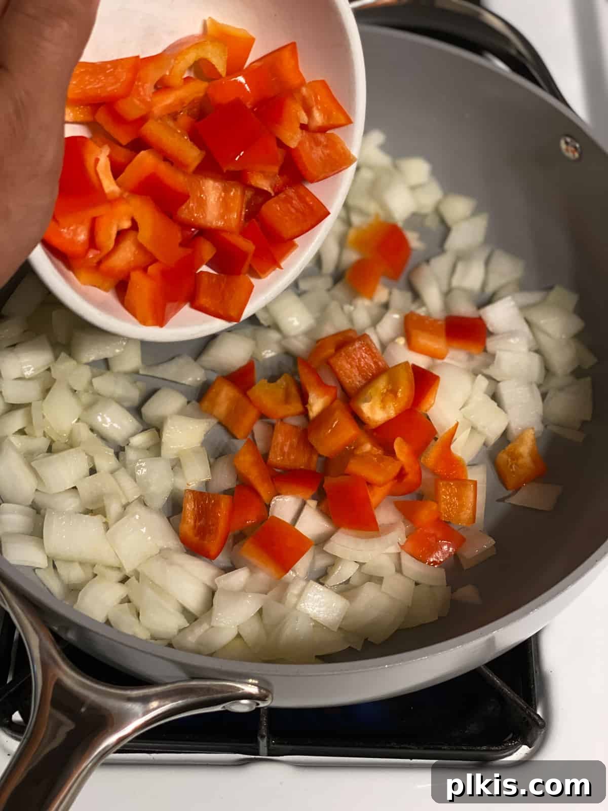 Vibrant Veggie Brown Rice Stir Fry 6 Process shot depicting diced red bell peppers being added to the pan with sautéing onions, adding color and flavor.
