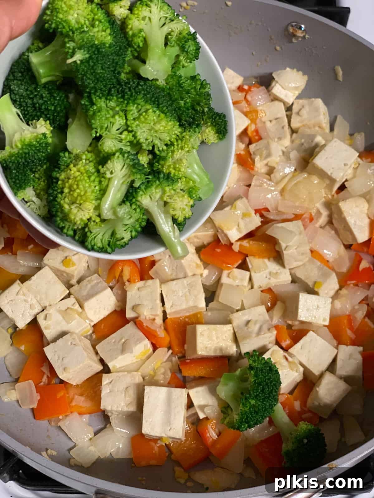 Vibrant Veggie Brown Rice Stir Fry 9 Process shot of frozen broccoli florets being introduced to the pan, ready to cook alongside other vegetables and tofu.