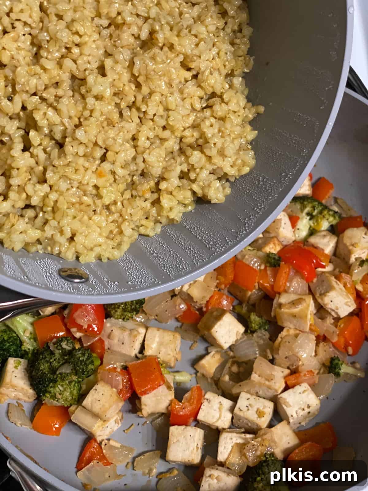 Vibrant Veggie Brown Rice Stir Fry 10 Process shot of fluffy brown rice being stirred into the skillet with sautéed vegetables and tofu, combining all ingredients for the final stir fry.