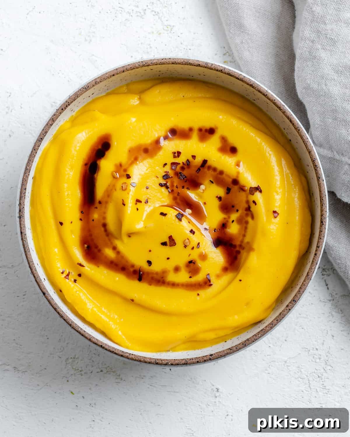 Creamy Vegan Pumpkin Dream 2 completed Easy Vegan Pumpkin Soup against a white surface, garnished with chili flakes and balsamic reduction