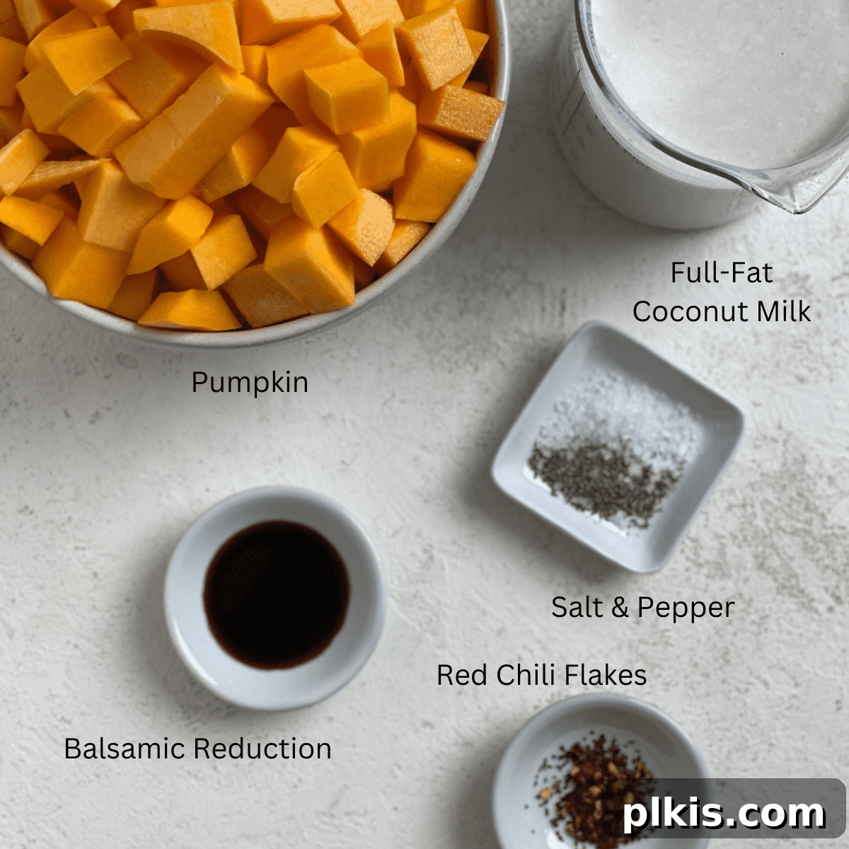 Creamy Vegan Pumpkin Dream 3 ingredients for Easy Vegan Pumpkin Soup measured out against a white surface, including pumpkin pieces, coconut milk, and chili flakes