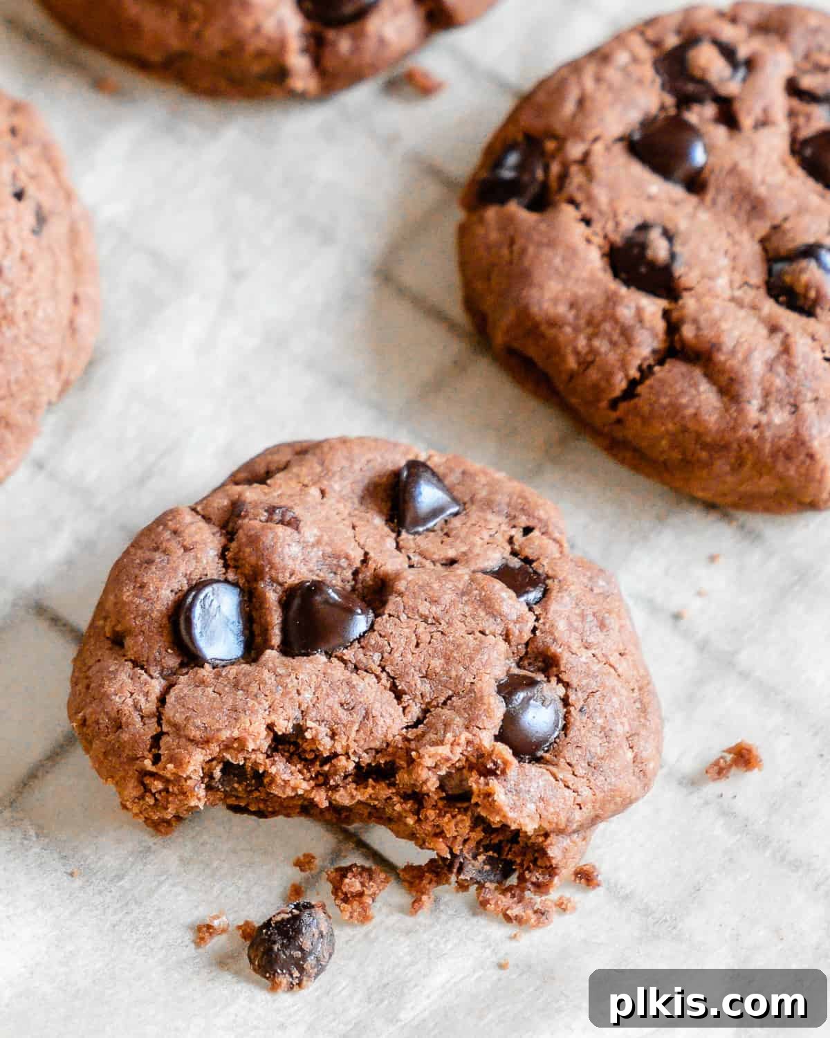 Peppermint Chocolate Chip Vegan Delights 2 Finished Vegan Double Chocolate Peppermint Cookies arranged on parchment paper, with one cookie halved to reveal its soft interior and chocolate chips.