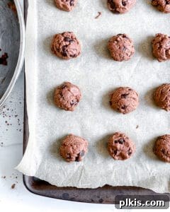 Peppermint Chocolate Chip Vegan Delights 7 Scoops of Chocolate Peppermint Chocolate Chip Cookie dough neatly placed on a baking sheet lined with parchment paper, ready for the oven.