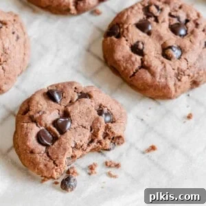 Finished Vegan Double Chocolate Peppermint Cookies arranged on parchment paper, with one cookie halved to reveal its soft interior and chocolate chips.