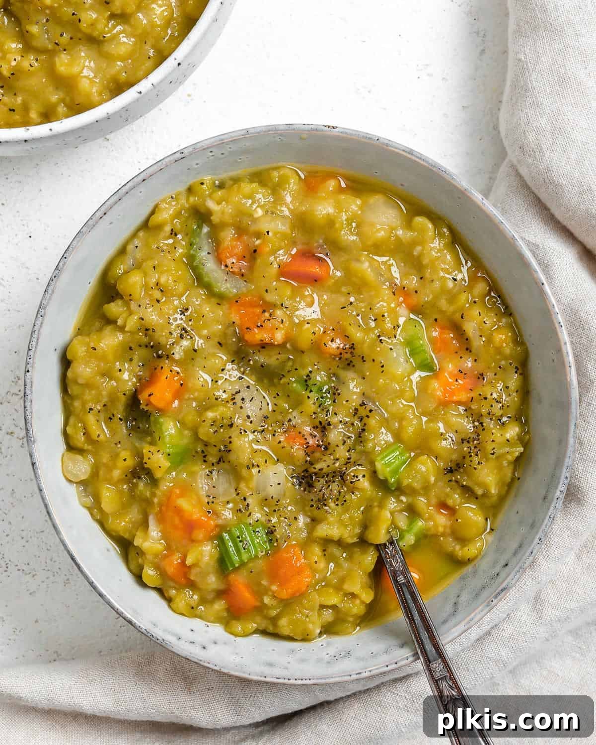 Golden Vegan Split Pea Goodness 2 A steaming bowl of rich, creamy Vegan Split Pea Soup garnished with fresh herbs, set against a rustic white surface.