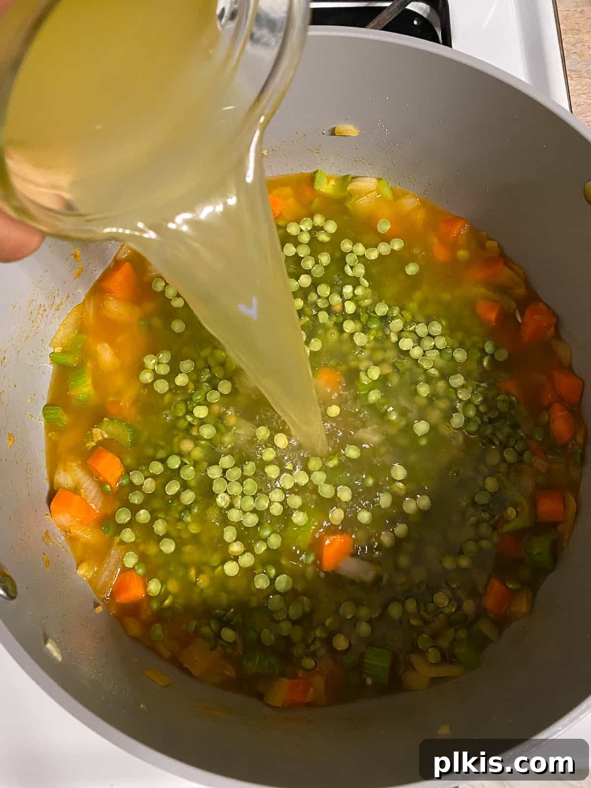 Golden Vegan Split Pea Goodness 5 A process shot showing vegetable broth being poured into a large soup pot filled with sautéed vegetables.