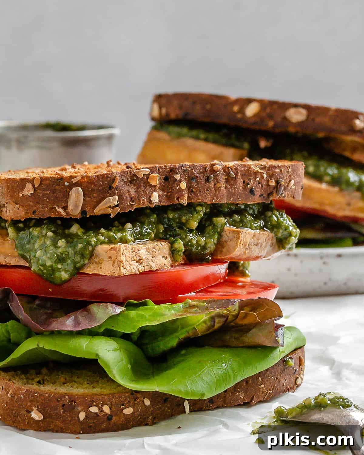 Pesto Tofu Sandwich: Simple Savory Superb 2 Two perfectly assembled vegan pesto tofu sandwiches, artfully arranged on a light surface, showcasing layers of roasted tofu, vibrant pesto, fresh lettuce, and ripe tomatoes. Ideal for a plant-based lunch or quick meal prep.