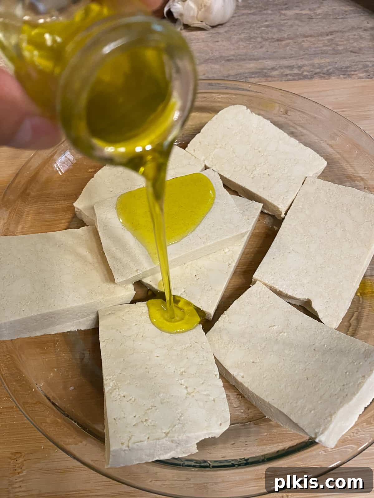 Pesto Tofu Sandwich: Simple Savory Superb 5 Sliced tofu pieces on a baking sheet being drizzled with extra virgin olive oil, preparing them for roasting and flavor infusion.
