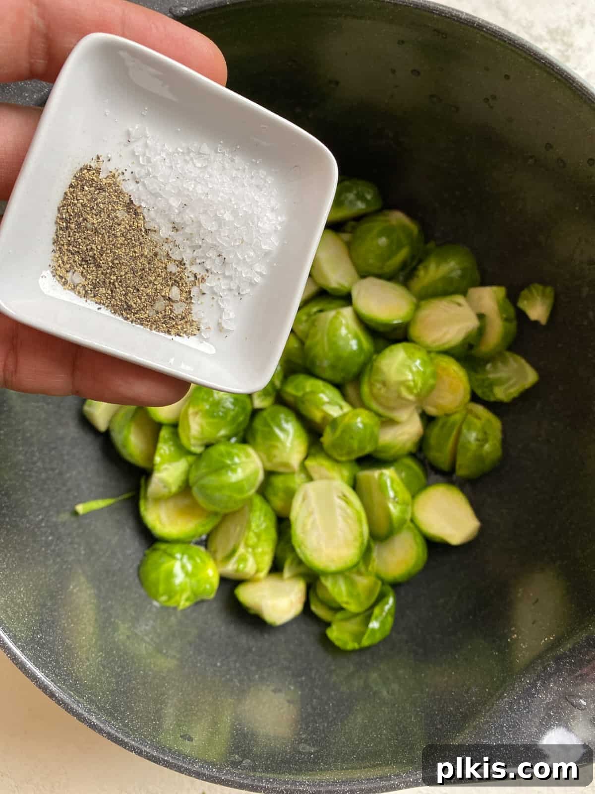 Tangy Cranberry Roasted Brussels Sprouts 5 Process shot of sprinkling salt and pepper onto Brussels sprouts on a baking sheet.