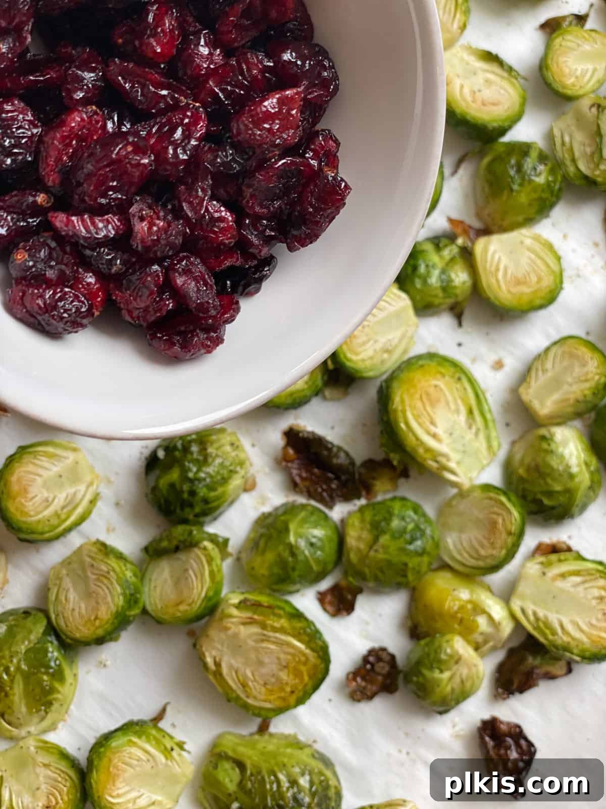 Tangy Cranberry Roasted Brussels Sprouts 8 Process shot of adding dried cranberries to roasted Brussels sprouts on a baking mat.