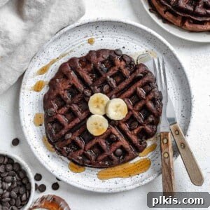 completed waffle on a white plate against a white background with syrup scattered on waffle