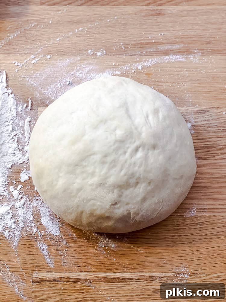 Simple Plant-Based Pizza Crust 6 Process shot showing a ball of smooth, elastic pizza dough on a lightly floured wooden surface