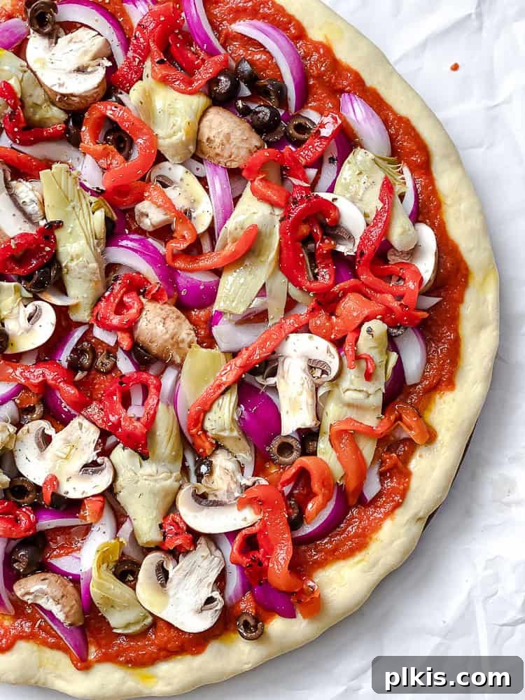 Simple Plant-Based Pizza Crust 8 Process shot showing colorful vegetables and vegan cheese toppings layered on a pizza dough