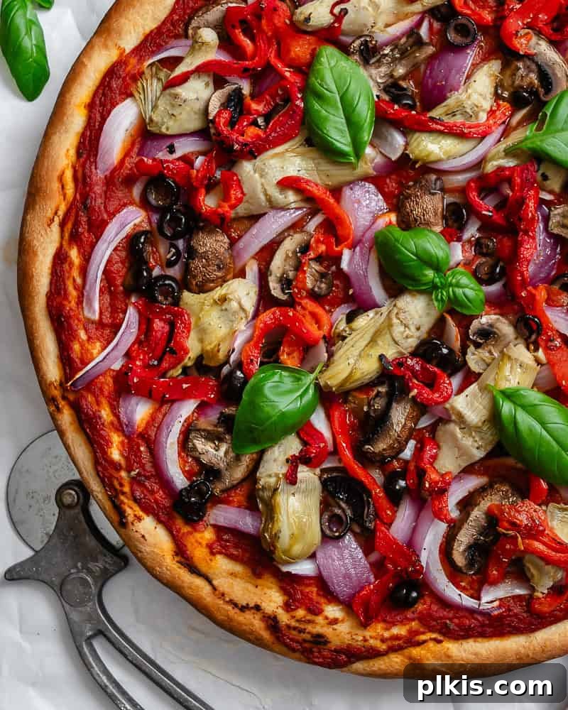 Simple Plant-Based Pizza Crust 9 Close-up of a completed Easy Vegan Pizza Dough pizza, adorned with colorful vegetables and melted vegan cheese, presented on a white surface