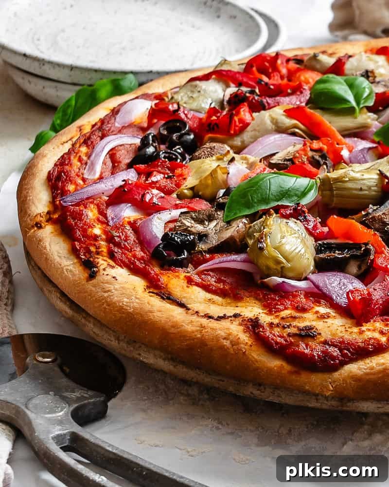 Simple Plant-Based Pizza Crust 10 A perfectly baked Easy Vegan Pizza Dough pizza, adorned with colorful vegetables and melted vegan cheese, presented on a white surface, ready to be sliced