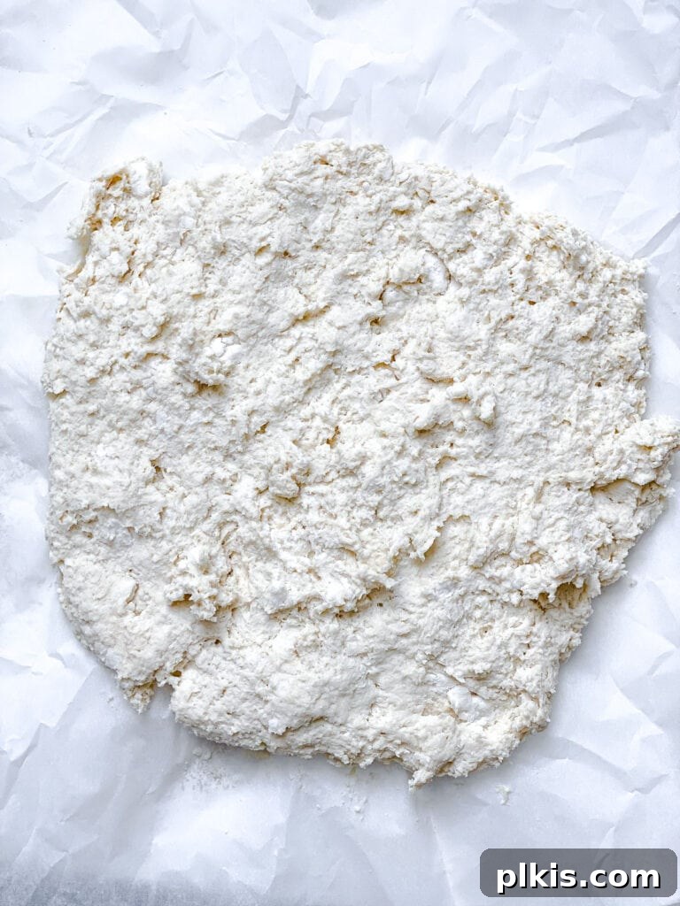 Effortless Plant-Based Biscuits in Minutes 11 Vegan biscuit dough is spread out on a lightly floured white surface, ready for folding to create layers.