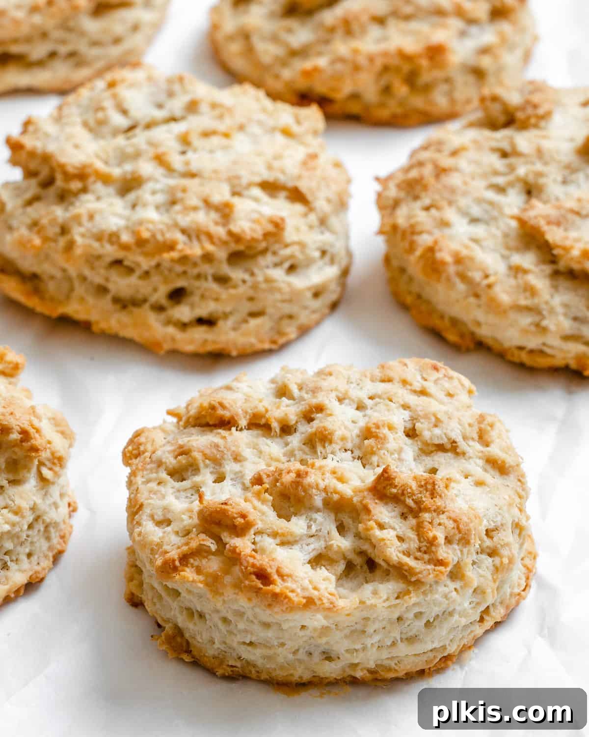 Effortless Plant-Based Biscuits in Minutes 14 A stack of golden-brown, flaky vegan buttermilk biscuits on a white surface, showcasing their delicious texture.