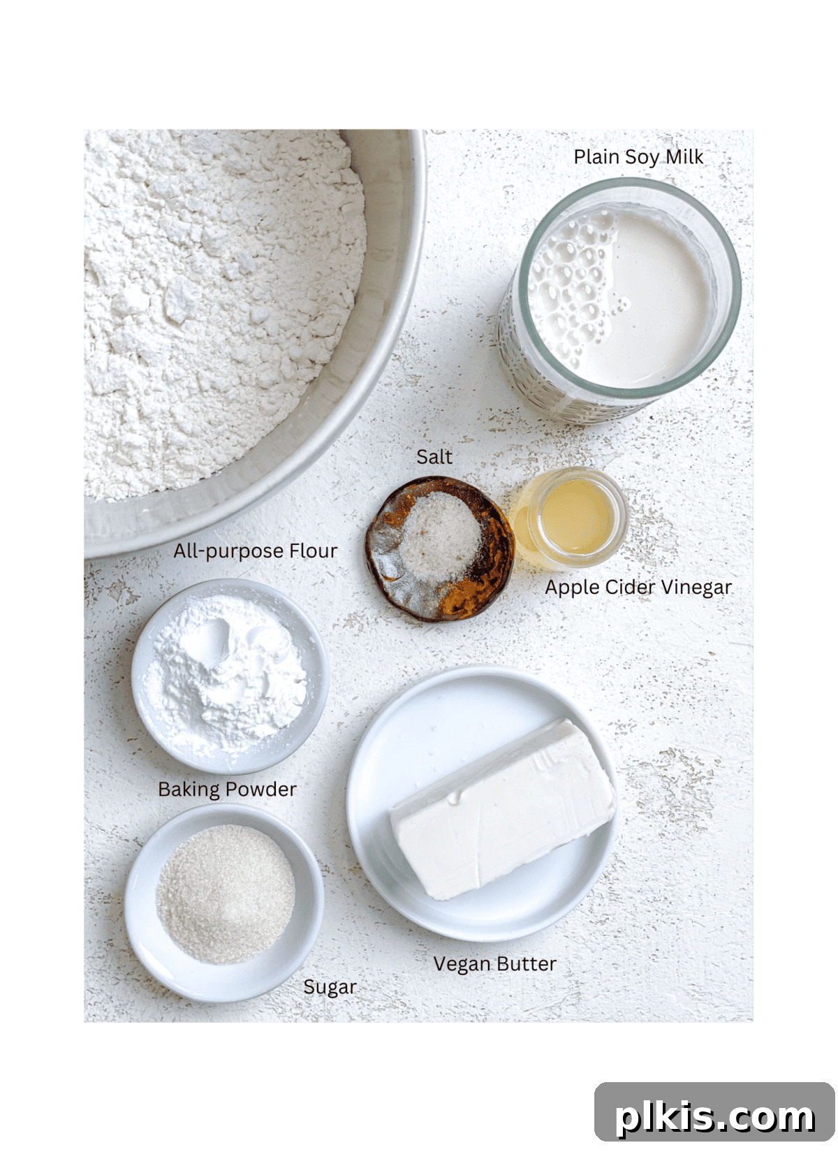 Effortless Plant-Based Biscuits in Minutes 3 A selection of measured ingredients for vegan biscuits laid out on a white background, including flour, vegan butter, plant milk, and vinegar.