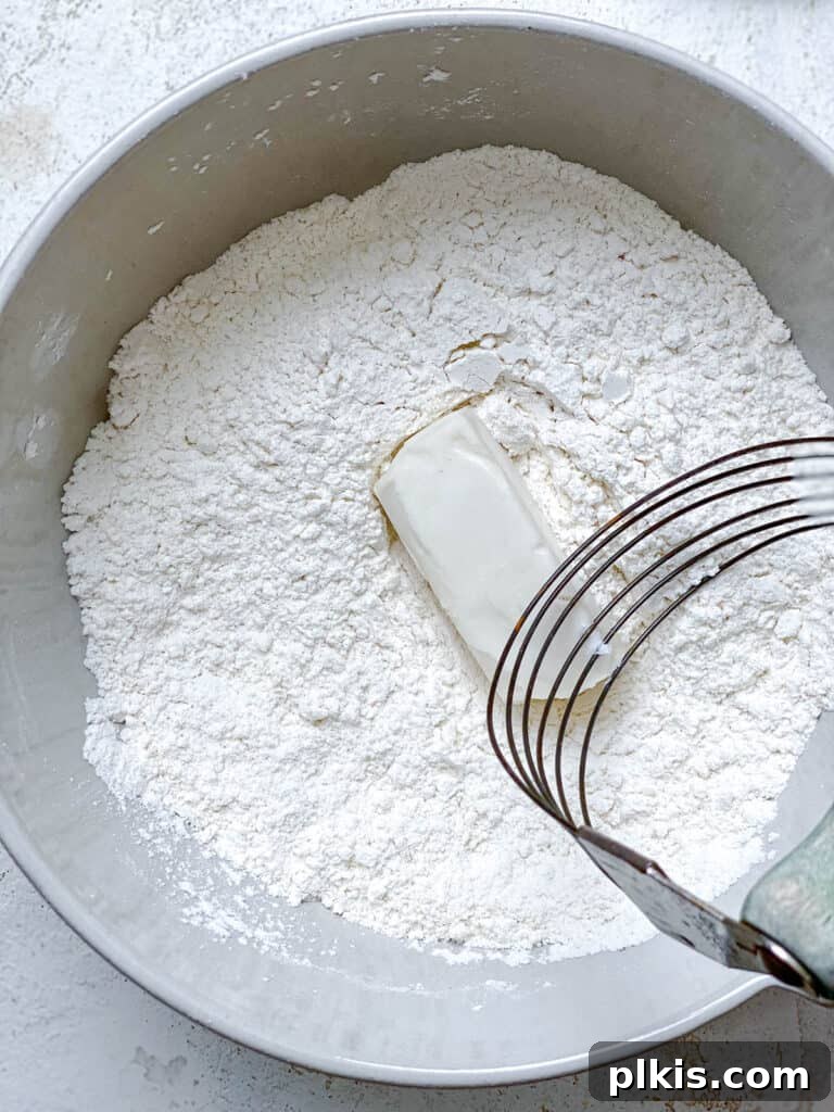 Effortless Plant-Based Biscuits in Minutes 7 Using a pastry cutter, frozen vegan butter is being cut into the flour mixture until it forms coarse crumbs.