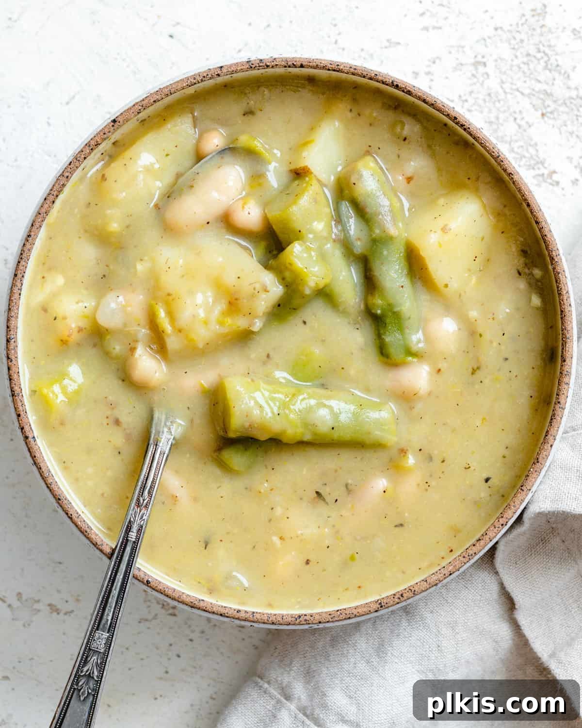 A beautifully presented bowl of creamy vegan asparagus soup garnished with fresh herbs and a drizzle of olive oil, ready to be enjoyed.