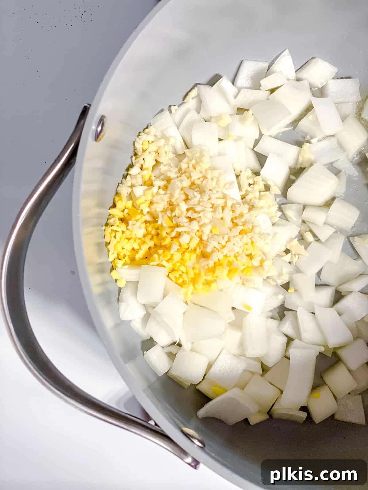 Process shot of diced onions, garlic, and ginger sautéing in a pot with oil, creating a fragrant base for the soup.
